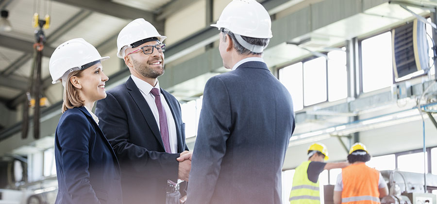 Businessmen shaking hands with workers working in background at metal industry